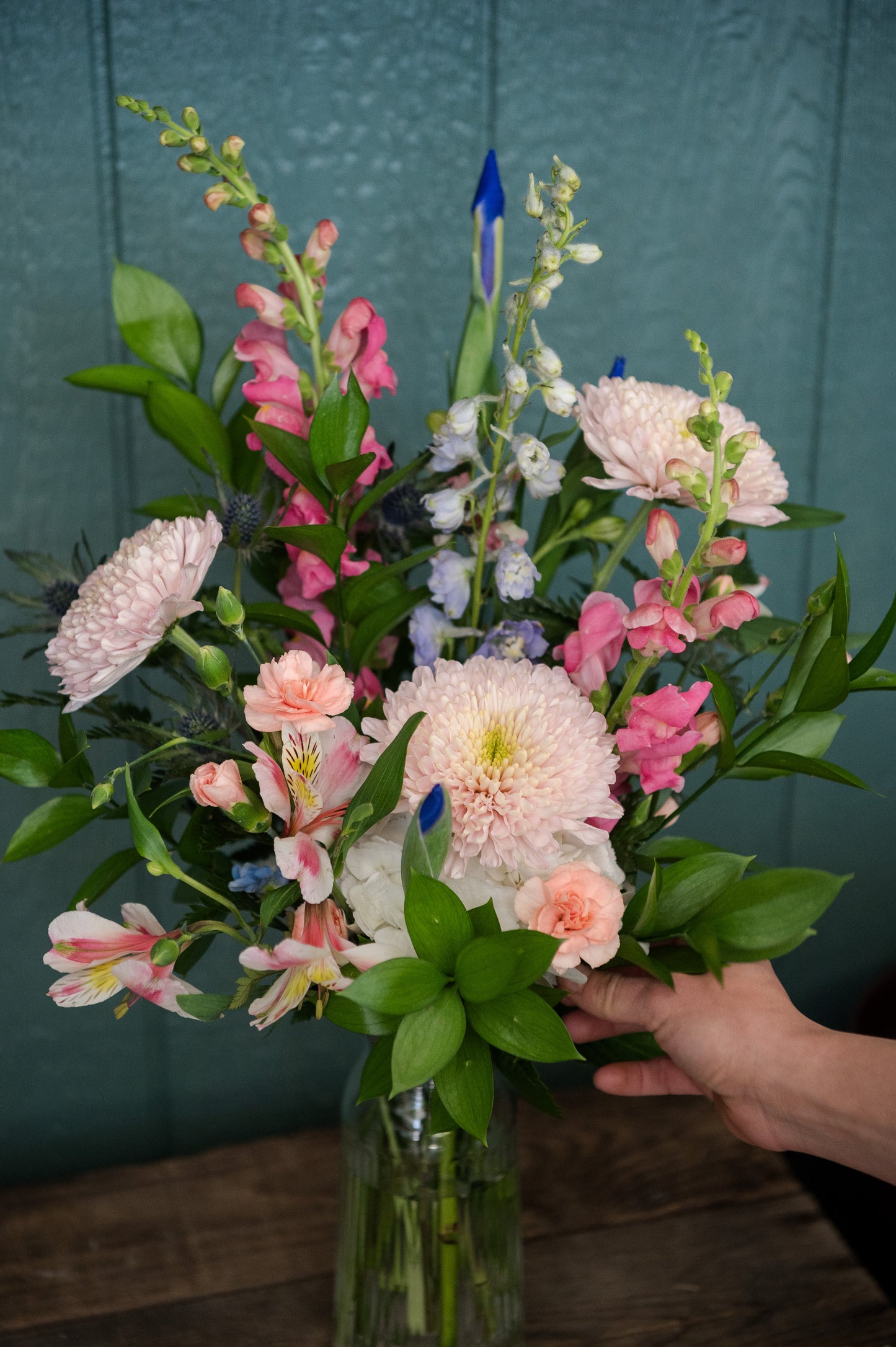Bouquet of flowers in a vase arranged by a hand against a teal background