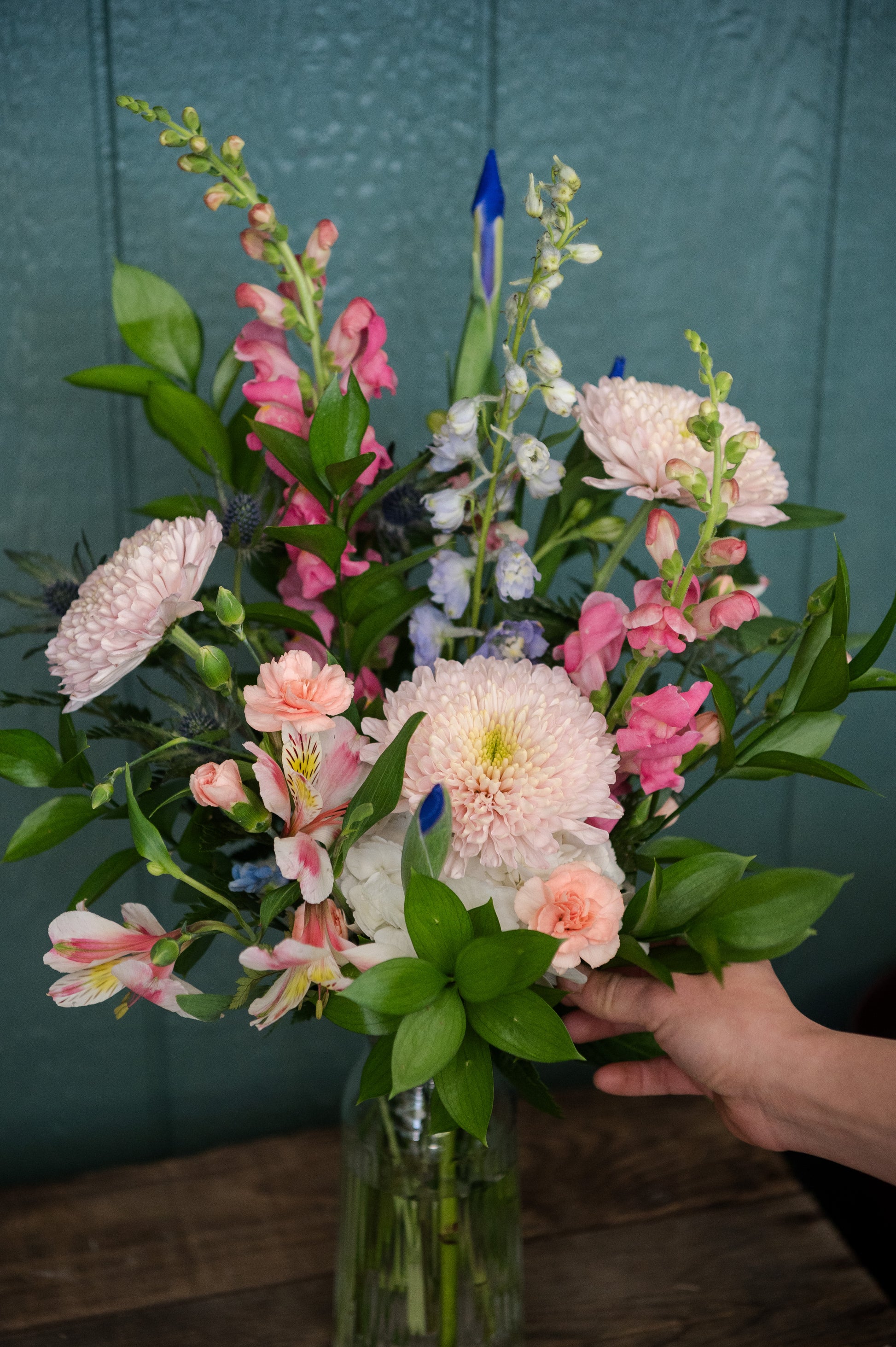 Bouquet of flowers in a vase arranged by a hand against a teal background
