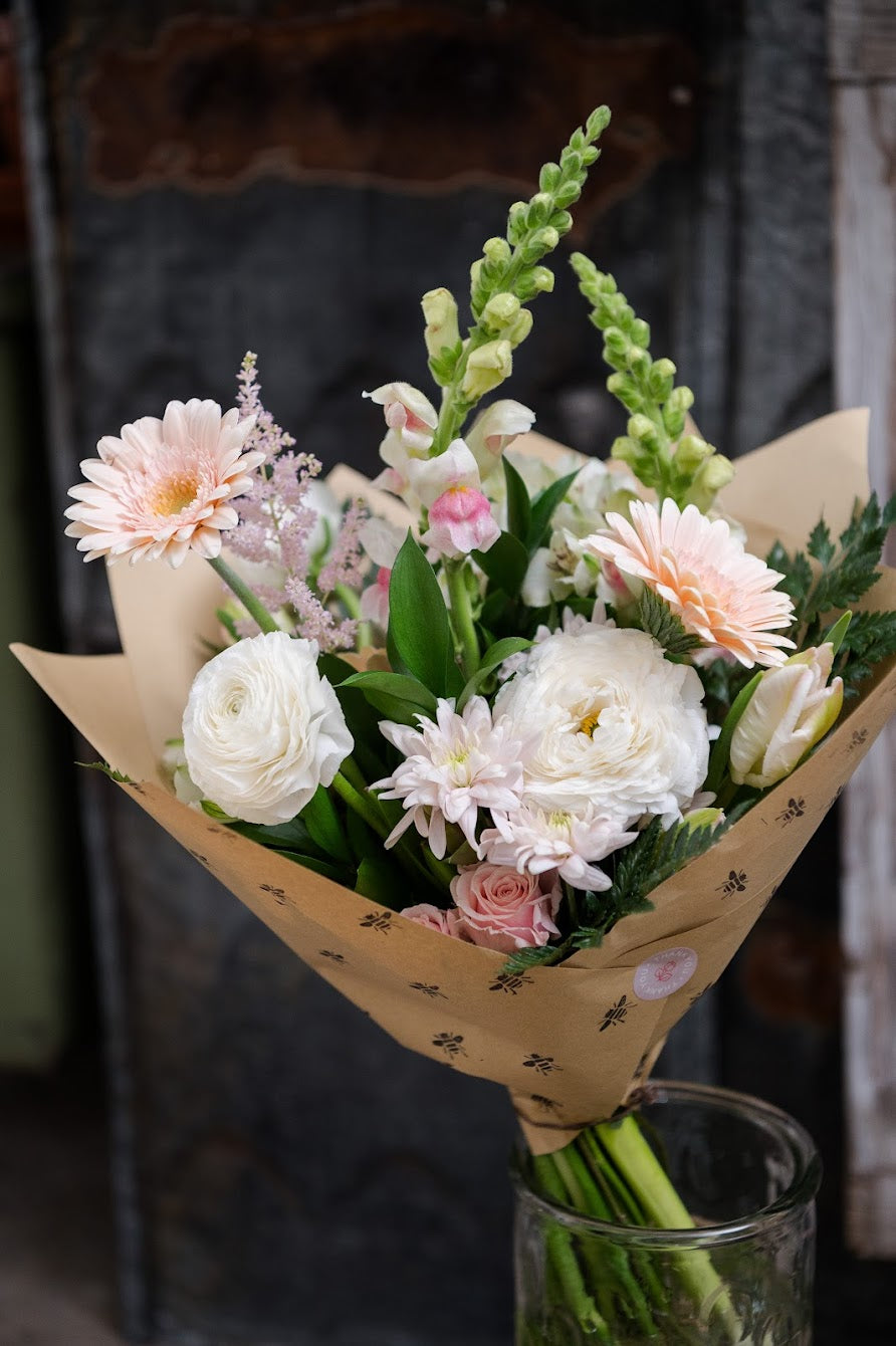 Bouquet of flowers wrapped in brown paper with a glass vase in the foreground.